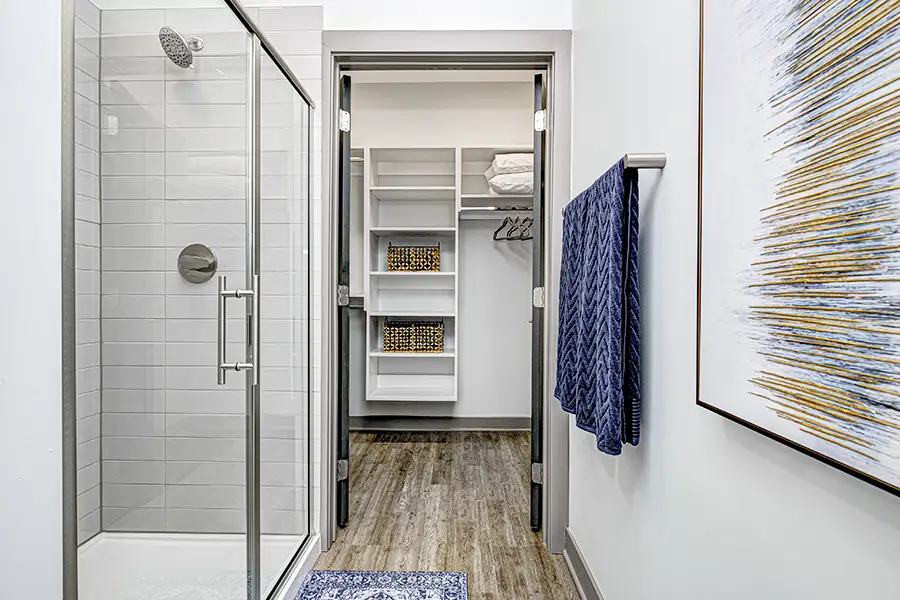 A windowless bathroom or closet like this space at The State at Fishers offers protection during inclement weather. A bathroom with a shower on the left and towel rack and abstract artwork on the right. Then facing an open walk in closet with shelving and hangers